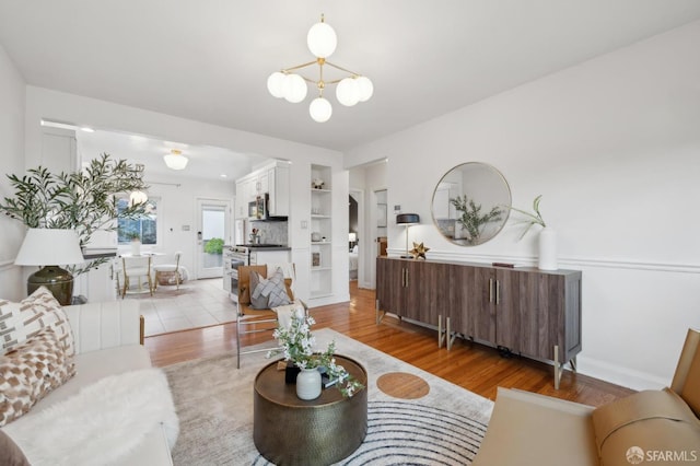 living room with light wood finished floors, built in shelves, baseboards, and an inviting chandelier