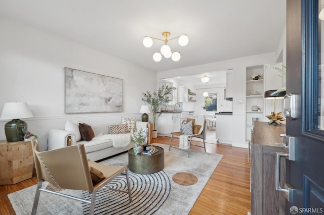 living room with built in shelves, light wood-style floors, and a chandelier