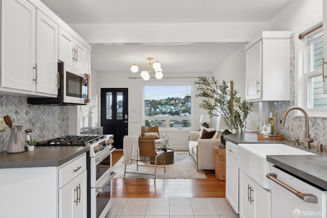 kitchen featuring white appliances, light tile patterned flooring, a sink, white cabinets, and dark countertops