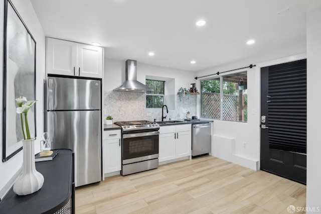 kitchen with a sink, dark countertops, white cabinetry, appliances with stainless steel finishes, and wall chimney exhaust hood