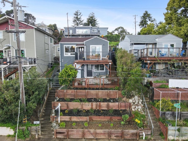 back of property featuring stairway, a wooden deck, and a garden