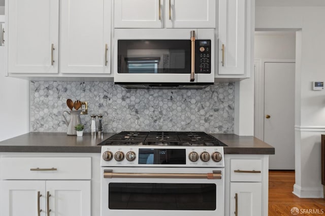 kitchen with backsplash, dark countertops, wood finished floors, white appliances, and white cabinets