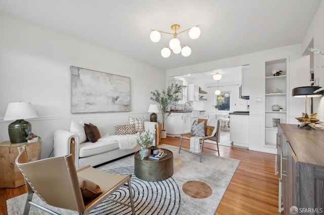 living area with built in shelves, light wood-type flooring, and an inviting chandelier