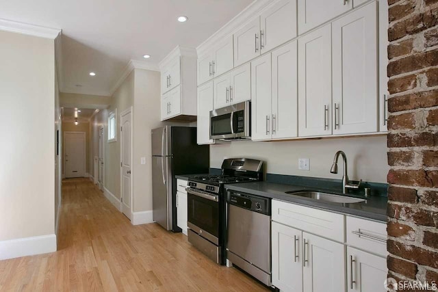 kitchen featuring dark countertops, appliances with stainless steel finishes, crown molding, white cabinetry, and a sink