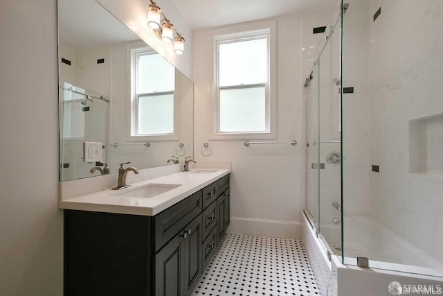 full bath featuring double vanity, a sink, baseboards, and bath / shower combo with glass door