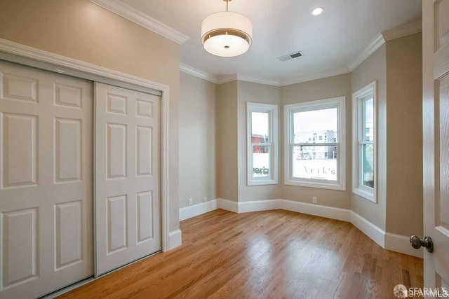 unfurnished bedroom featuring crown molding, light wood finished floors, a closet, visible vents, and baseboards