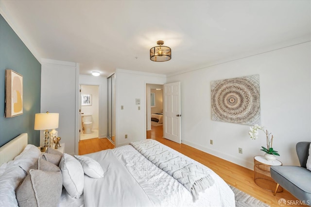 bedroom with ensuite bath, baseboards, and wood finished floors