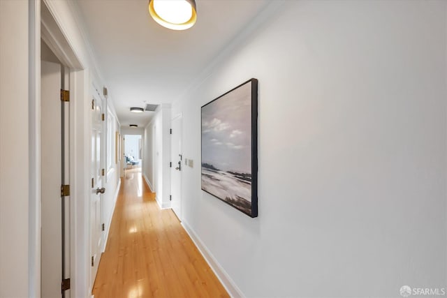 corridor with light wood-type flooring, visible vents, baseboards, and crown molding