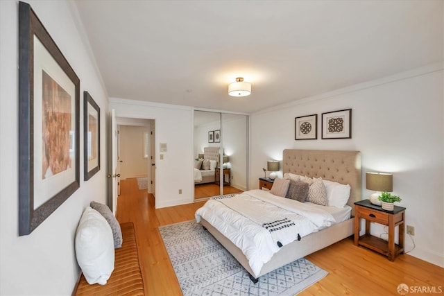 bedroom with light wood-style floors, baseboards, a closet, and ornamental molding