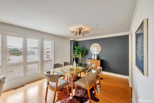 dining area featuring light wood-type flooring, baseboards, visible vents, and crown molding