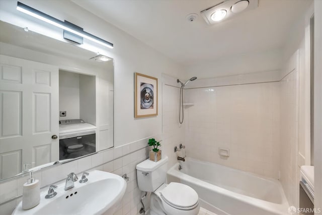 bathroom featuring tile walls, washer / clothes dryer, bathtub / shower combination, toilet, and a sink