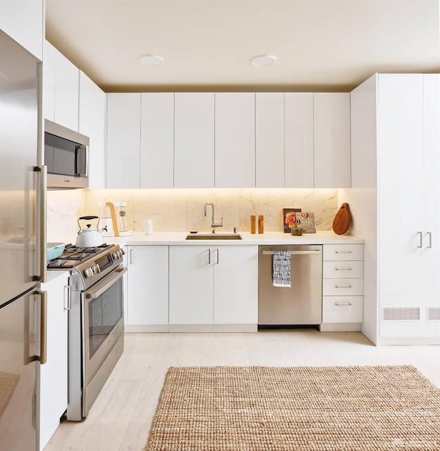 kitchen with white cabinets, backsplash, sink, and stainless steel appliances