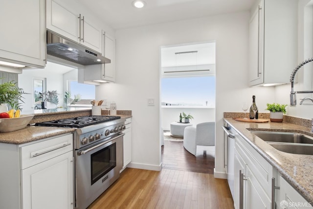 kitchen featuring a sink, under cabinet range hood, stainless steel range, light wood-style flooring, and white cabinetry