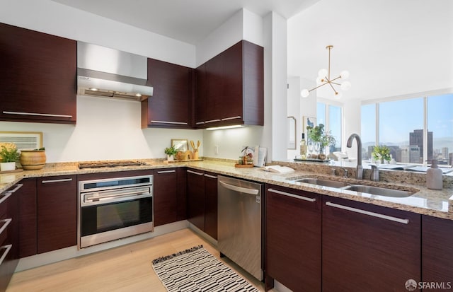 kitchen featuring modern cabinets, wall chimney range hood, a sink, light wood-style flooring, and stainless steel appliances