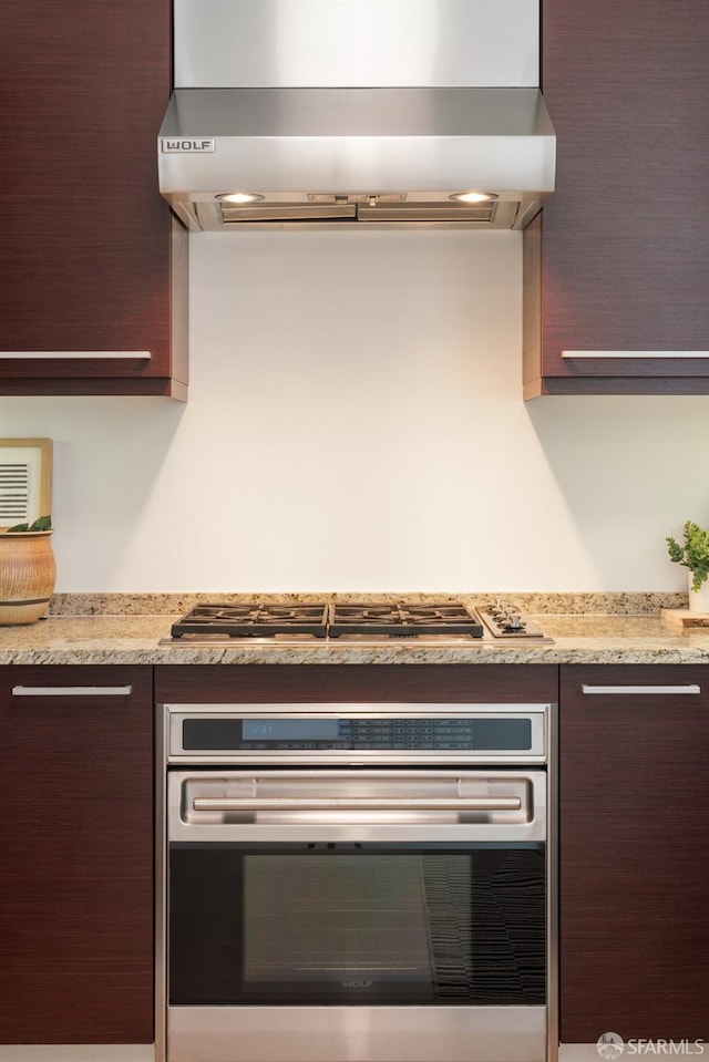 kitchen featuring wall chimney range hood, stainless steel appliances, dark brown cabinetry, and light countertops