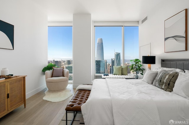 bedroom featuring a view of city, baseboards, multiple windows, and wood finished floors