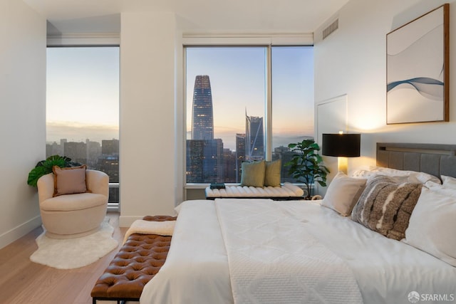 bedroom featuring multiple windows, baseboards, wood finished floors, visible vents, and a city view
