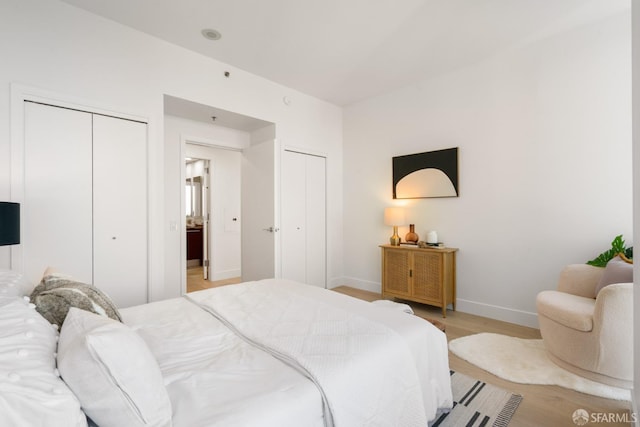 bedroom with two closets, baseboards, and light wood-style flooring