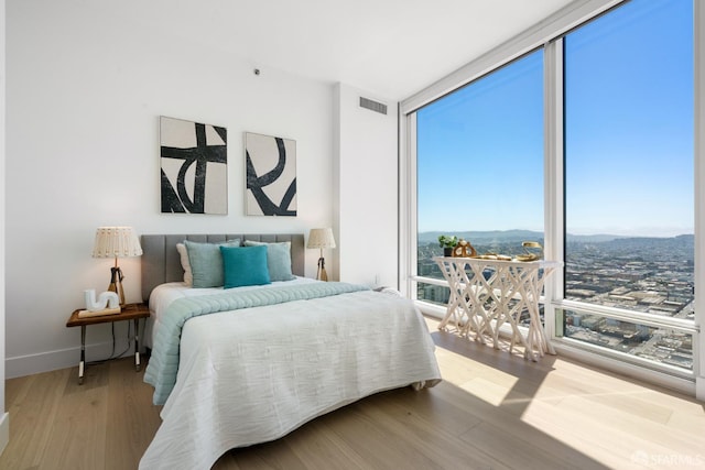 bedroom with visible vents, baseboards, wood finished floors, and expansive windows