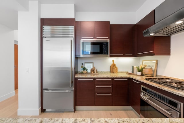 kitchen featuring modern cabinets, light stone counters, ventilation hood, light wood-style floors, and built in appliances