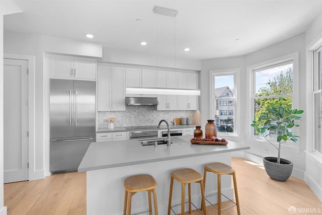 38 Steiner St Unit 303, San Francisco, CA 94114 - kitchen with stainless steel built in fridge, under cabinet range hood, light wood-style floors, tasteful backsplash, and white cabinetry