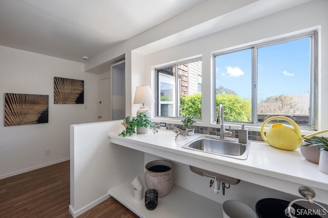 kitchen featuring dark wood-style floors, light countertops, a sink, a kitchen breakfast bar, and baseboards