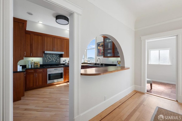 kitchen with gas stovetop, a sink, light wood-type flooring, oven, and under cabinet range hood