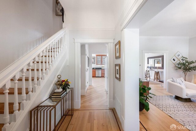 corridor with visible vents, a towering ceiling, stairway, crown molding, and light wood-type flooring