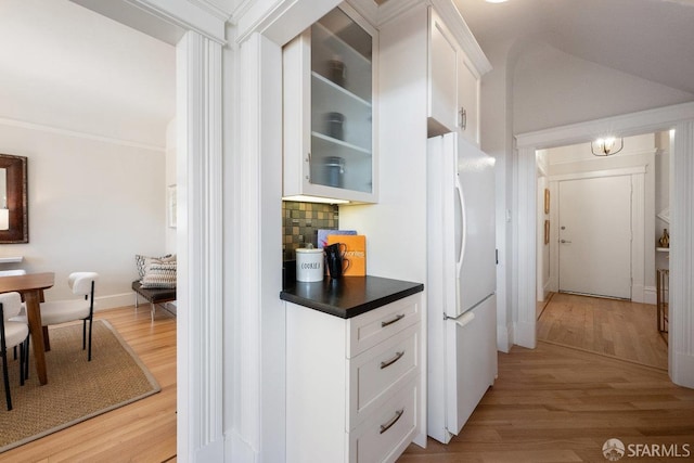 kitchen featuring white cabinets, light wood-type flooring, freestanding refrigerator, tasteful backsplash, and glass insert cabinets