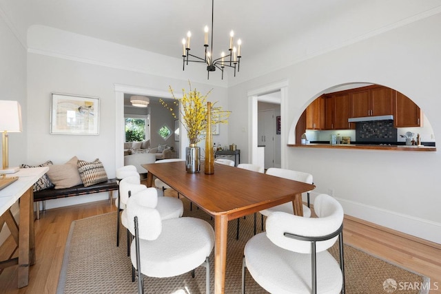 dining room with ornamental molding, light wood-style flooring, and an inviting chandelier