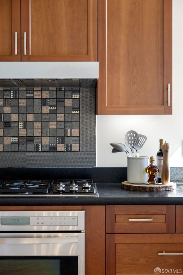 kitchen featuring brown cabinetry, decorative backsplash, dark countertops, gas stovetop, and stainless steel oven