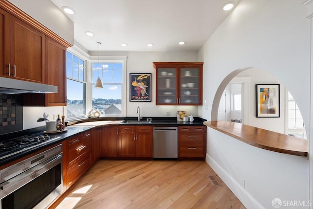 kitchen with dark countertops, a sink, oven, dishwasher, and under cabinet range hood