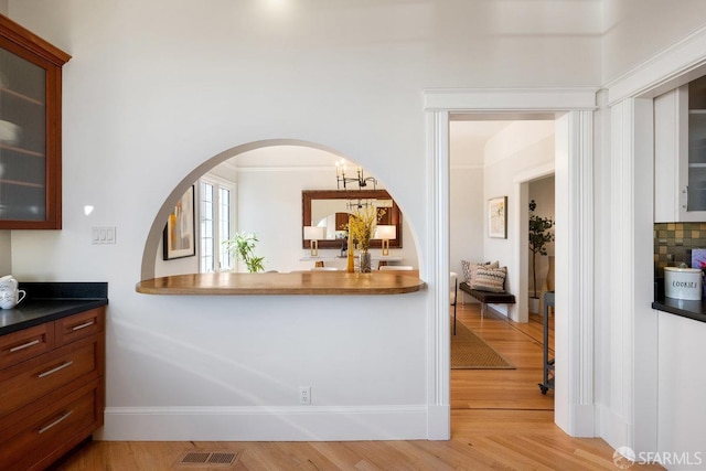 kitchen with visible vents, arched walkways, dark countertops, glass insert cabinets, and light wood-type flooring