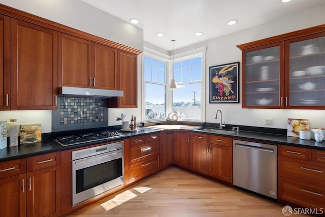 kitchen featuring stainless steel appliances, dark countertops, hanging light fixtures, a sink, and under cabinet range hood