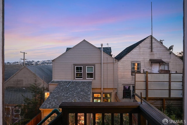 back of house at dusk with a shingled roof