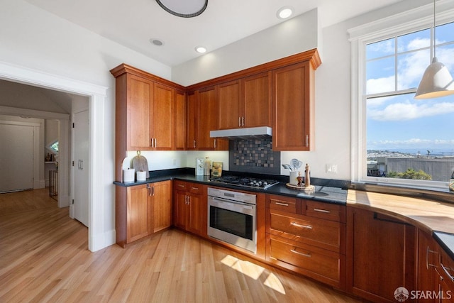 kitchen with under cabinet range hood, stainless steel appliances, light wood finished floors, and brown cabinetry