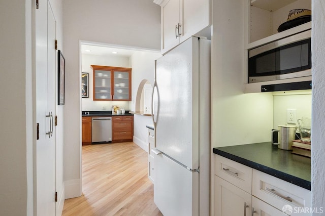 kitchen with light wood-type flooring, appliances with stainless steel finishes, dark countertops, and white cabinets