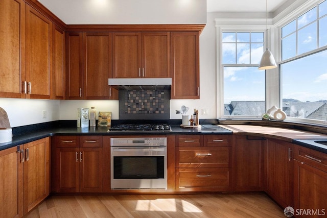 kitchen featuring dark countertops, under cabinet range hood, appliances with stainless steel finishes, and brown cabinetry