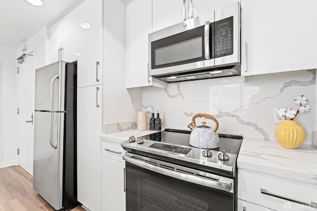 250 King St Unit 536, San Francisco, CA 94107 - kitchen with appliances with stainless steel finishes, white cabinets, light wood-style floors, light stone counters, and decorative backsplash