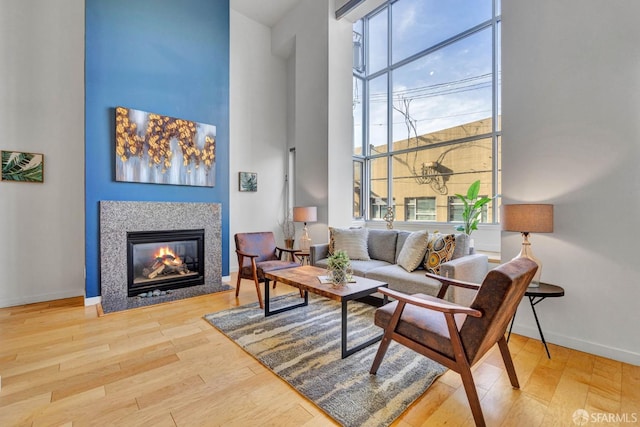 living room featuring wood finished floors, a high ceiling, a glass covered fireplace, and baseboards