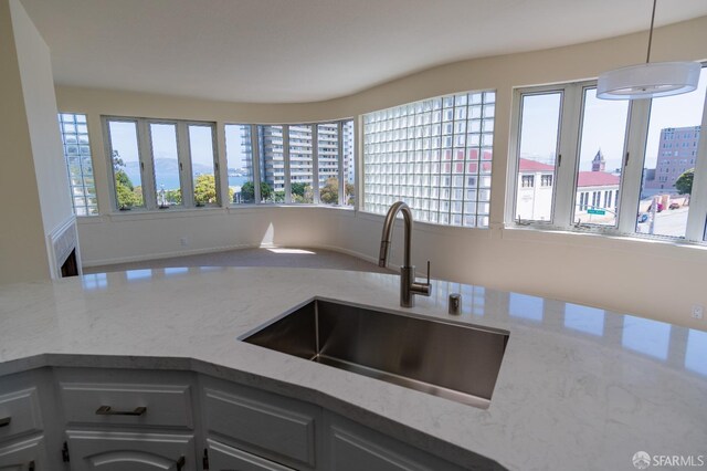kitchen featuring a sink, a view of city, decorative light fixtures, and light stone counters