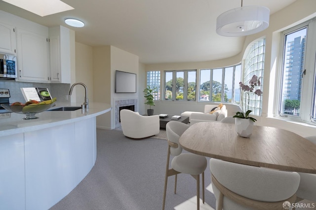 kitchen featuring white cabinets, a sink, light countertops, stainless steel microwave, and light carpet