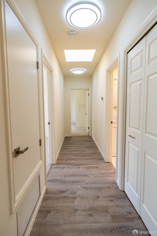 hall featuring visible vents, a skylight, wood finished floors, and baseboards