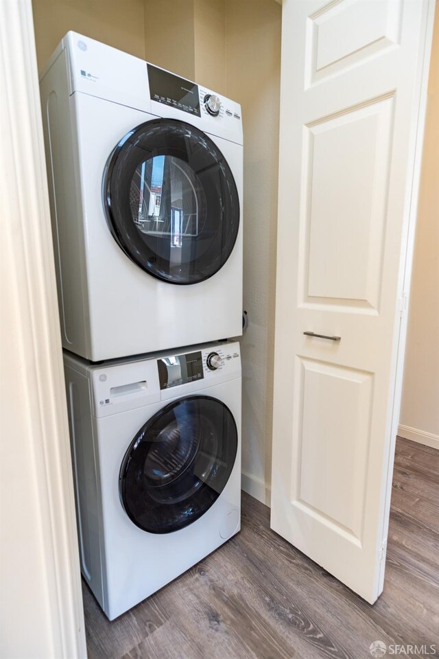 laundry room featuring laundry area, stacked washer and dryer, wood finished floors, and baseboards