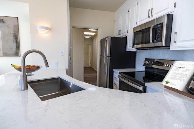 kitchen with light stone counters, a sink, white cabinets, and stainless steel appliances