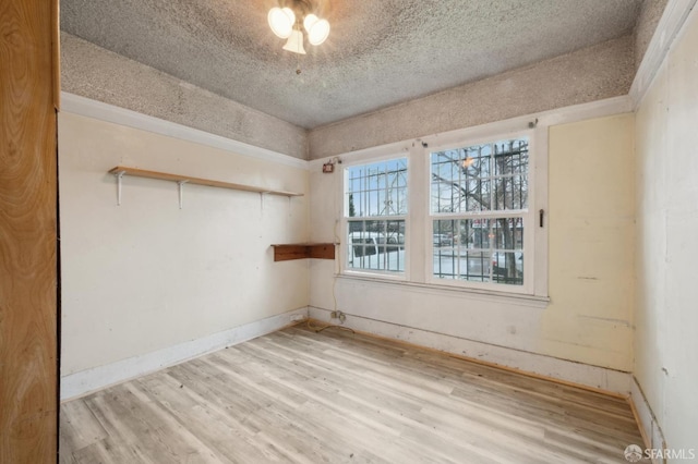 unfurnished room featuring light wood-style floors, baseboards, and a textured ceiling