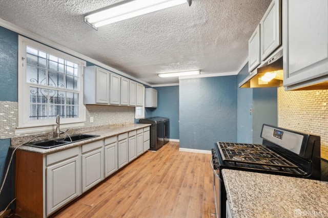 kitchen with tasteful backsplash, washer and clothes dryer, gas range, light wood-style flooring, and a sink