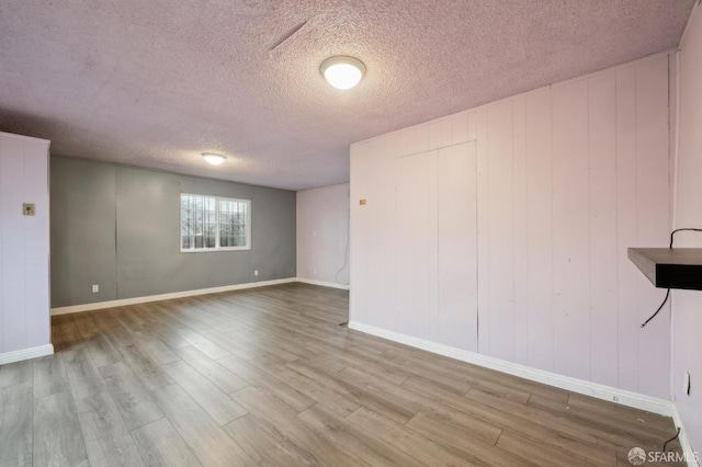 unfurnished room with baseboards, a textured ceiling, and light wood-style floors