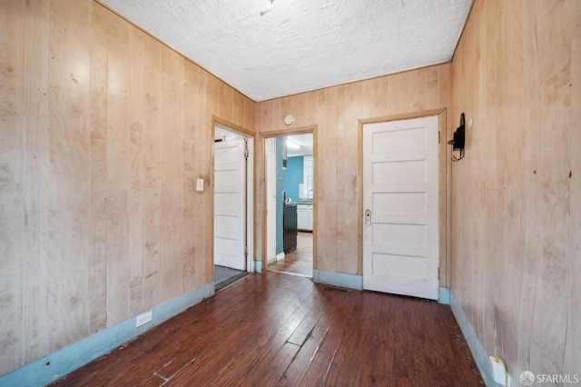 unfurnished room with a textured ceiling, wood walls, dark wood finished floors, and baseboards