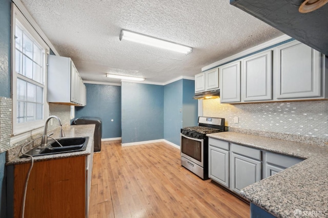 kitchen featuring tasteful backsplash, light wood-style floors, stainless steel range with gas stovetop, under cabinet range hood, and a sink